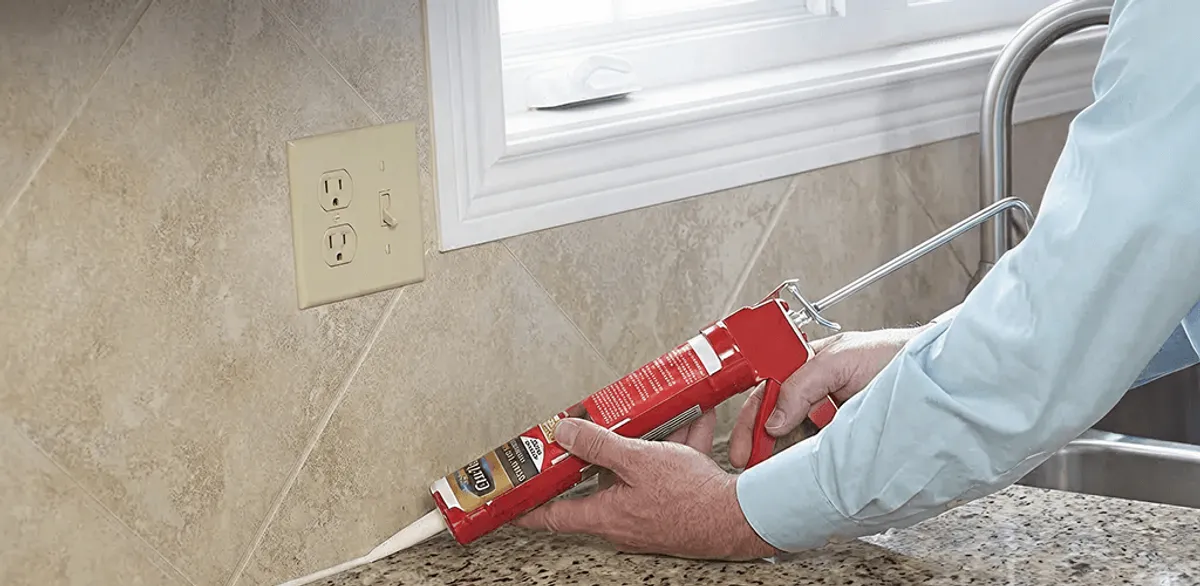 Handyman applying caulk along a kitchen backsplash and countertop seam in Columbus, OH